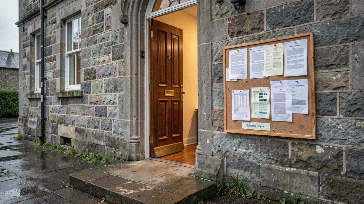 The open door of a grey stone parish hall in Aberdeen on a wet morning, light spilling onto the step, a noticeboard with pinned sheets beside it.